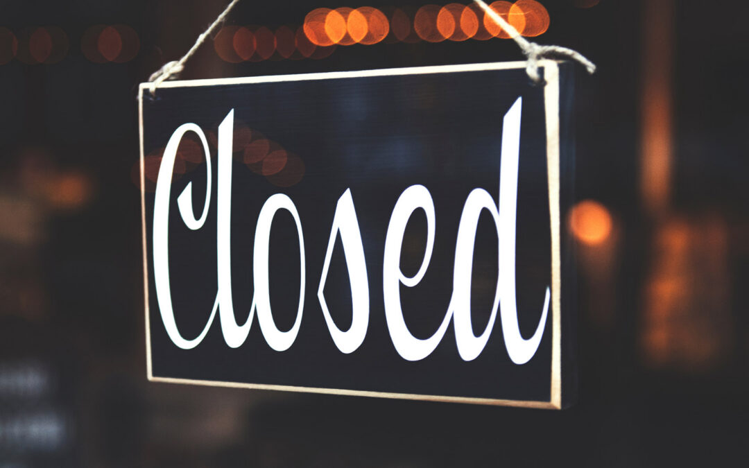 A hanging, black rectangular sign with a thin white border and the word "Closed" written in a large, elegant white script - https://www.staplesagency.com/