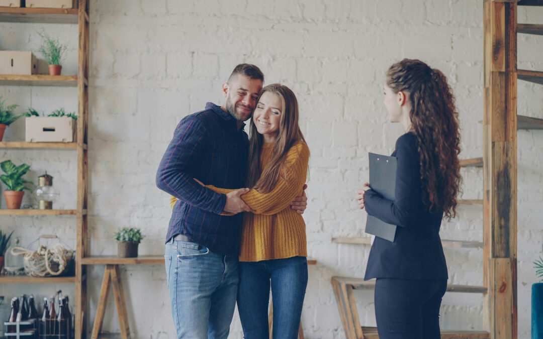 A smiling young couple embracing in a modern, loft-style apartment - https://www.staplesagency.com/