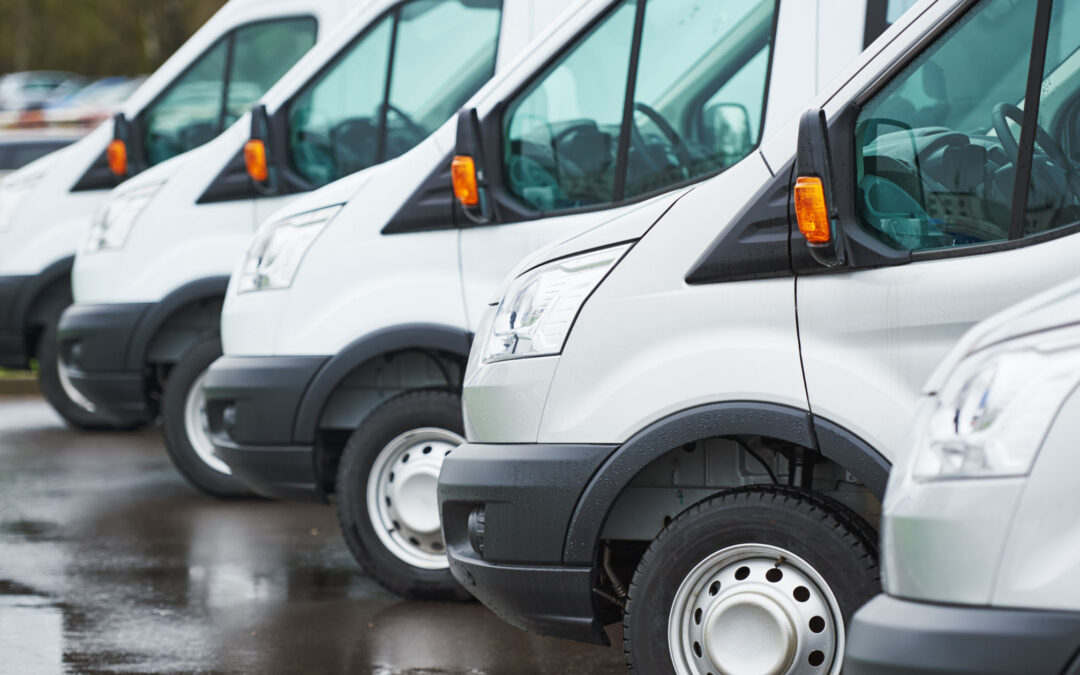 Row of white delivery vans parked on wet pavement.