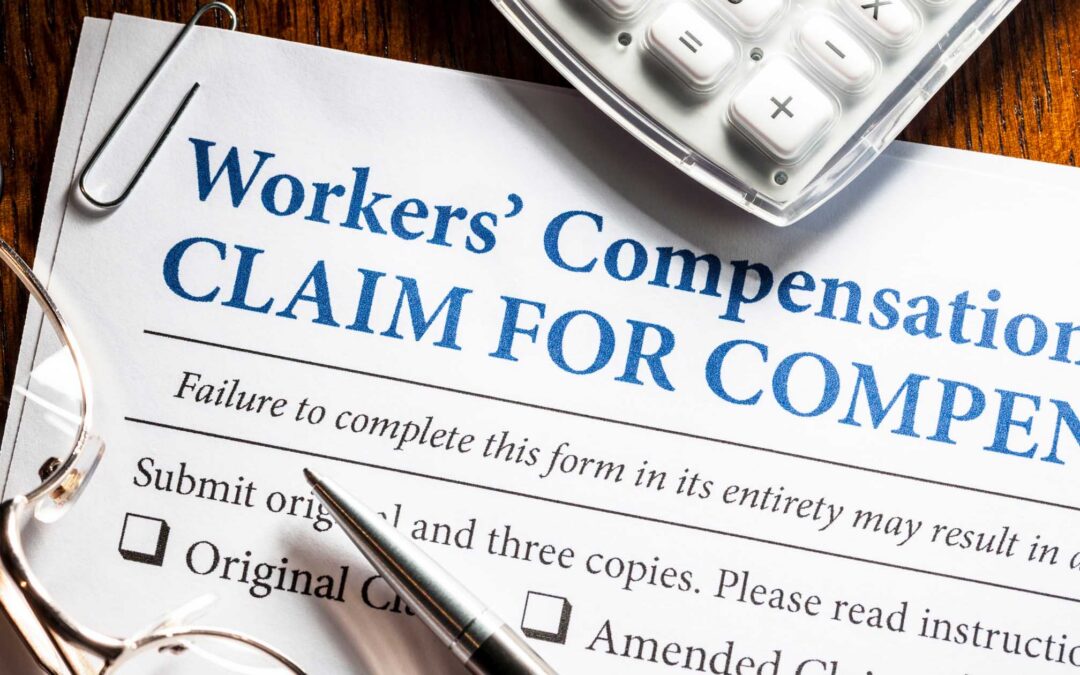 Close-up of a printed Workers' Compensation claim form with a pen, paperclip and calculator on a wooden desk.