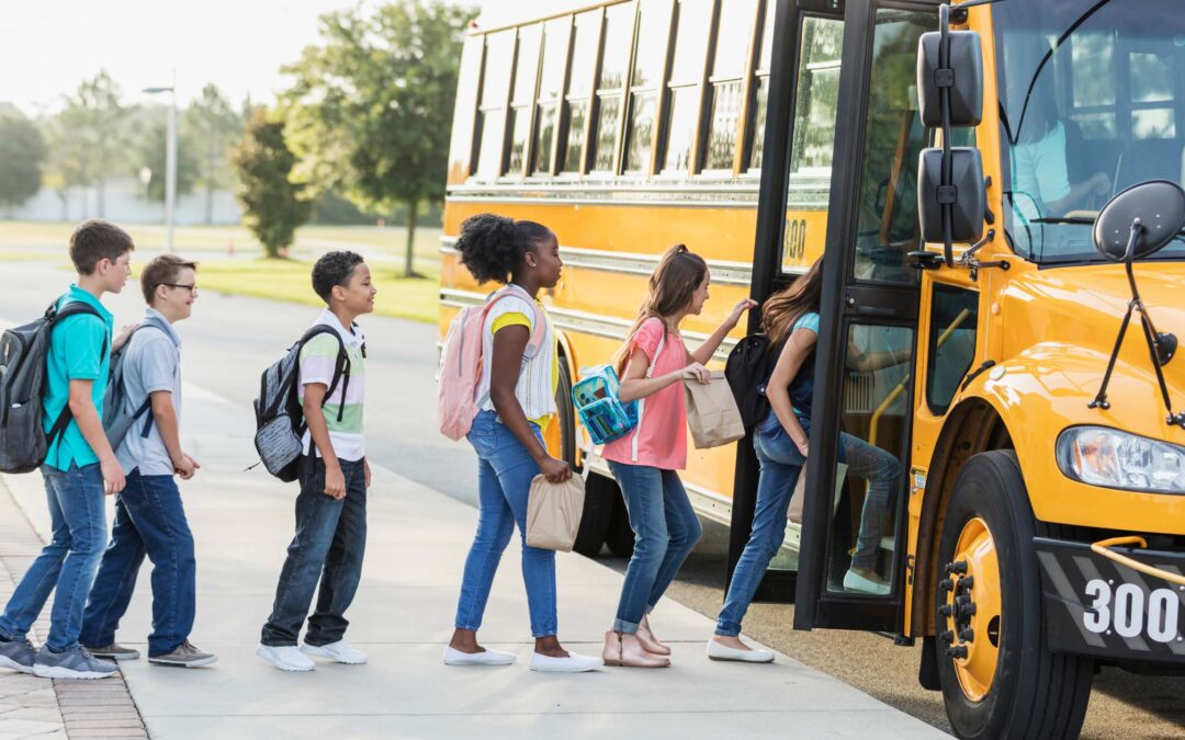 Schoolchildren with backpacks boarding a yellow school bus.