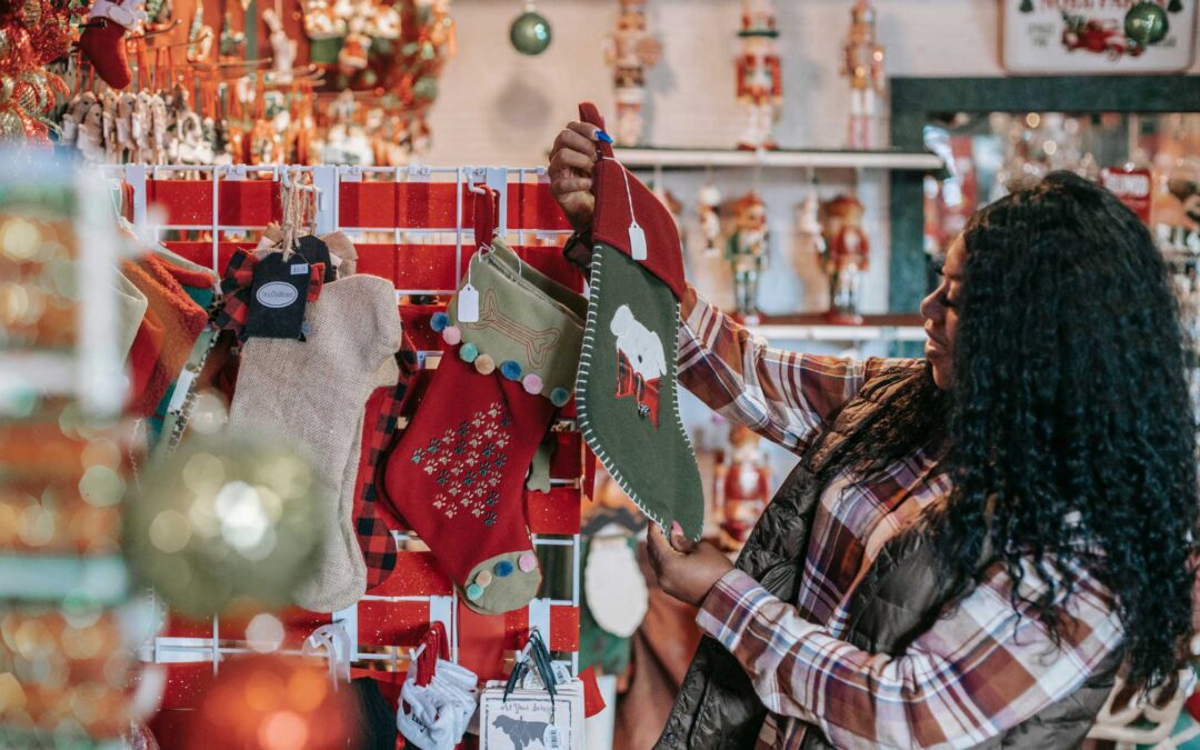 A woman in a plaid shirt examines colorful Christmas stockings in a festive store - staplesagency.com
