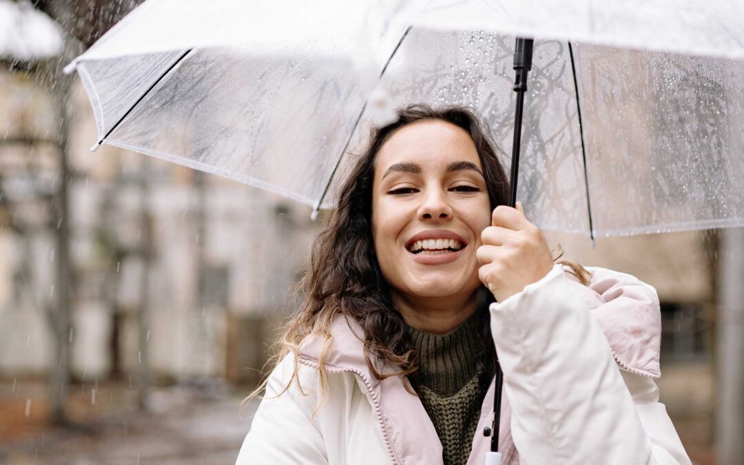 Smiling woman in a white coat holds a transparent umbrella on a rainy day