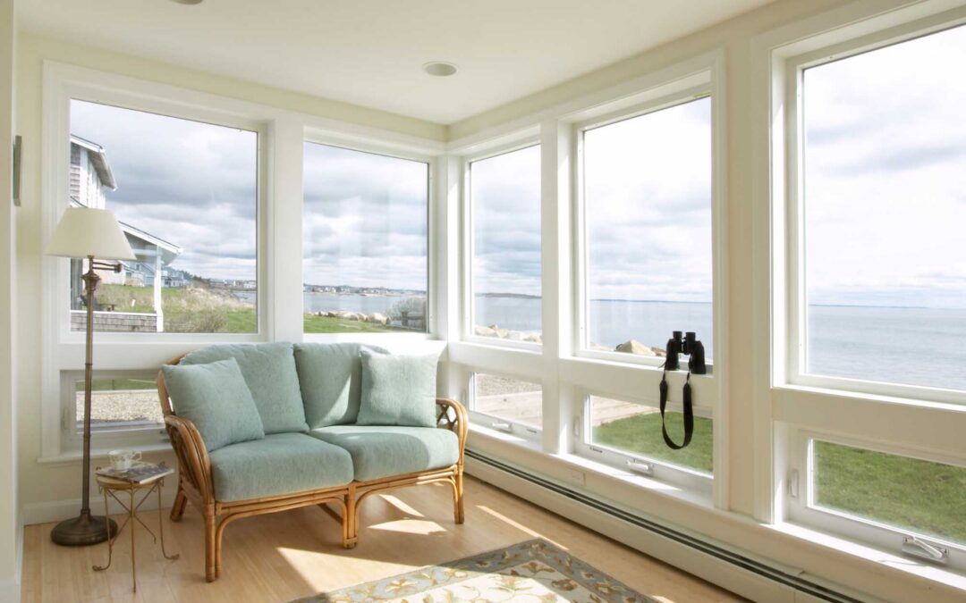 A cozy sunroom with large windows overlooking a calm sea - staplesagency.com