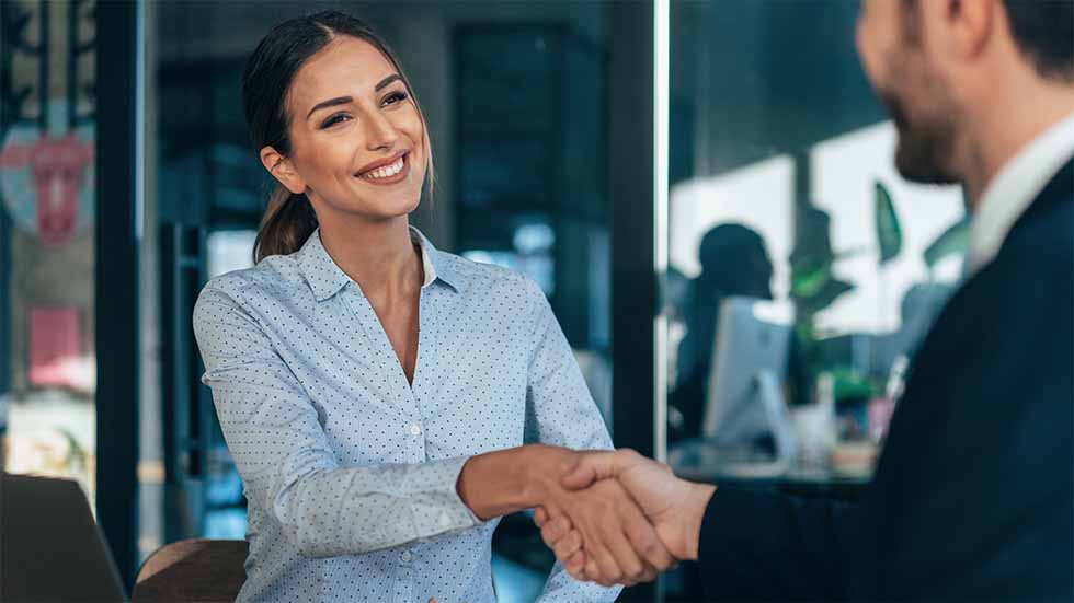 A professionally dressed businesswoman shaking hands with a businessman - staplesagency.com