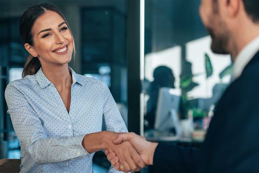 A professionally dressed businesswoman shaking hands with a businessman - staplesagency.com