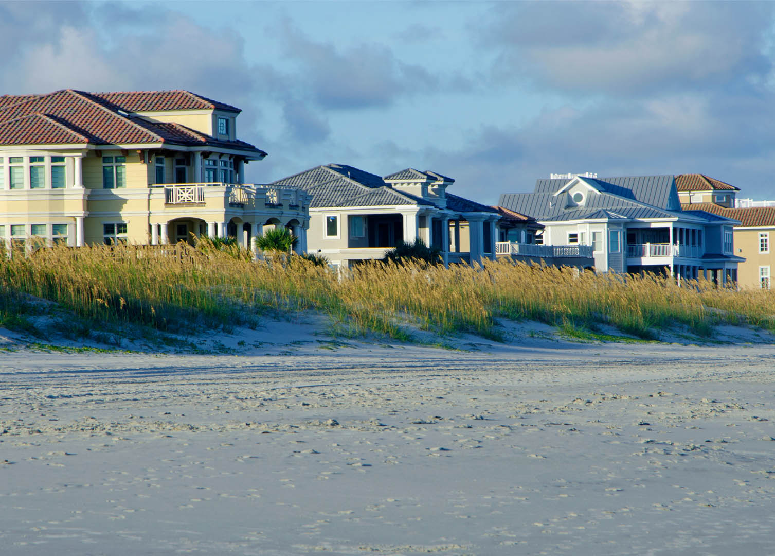 A row of beach-front homes with dunes and sand as their backyards.