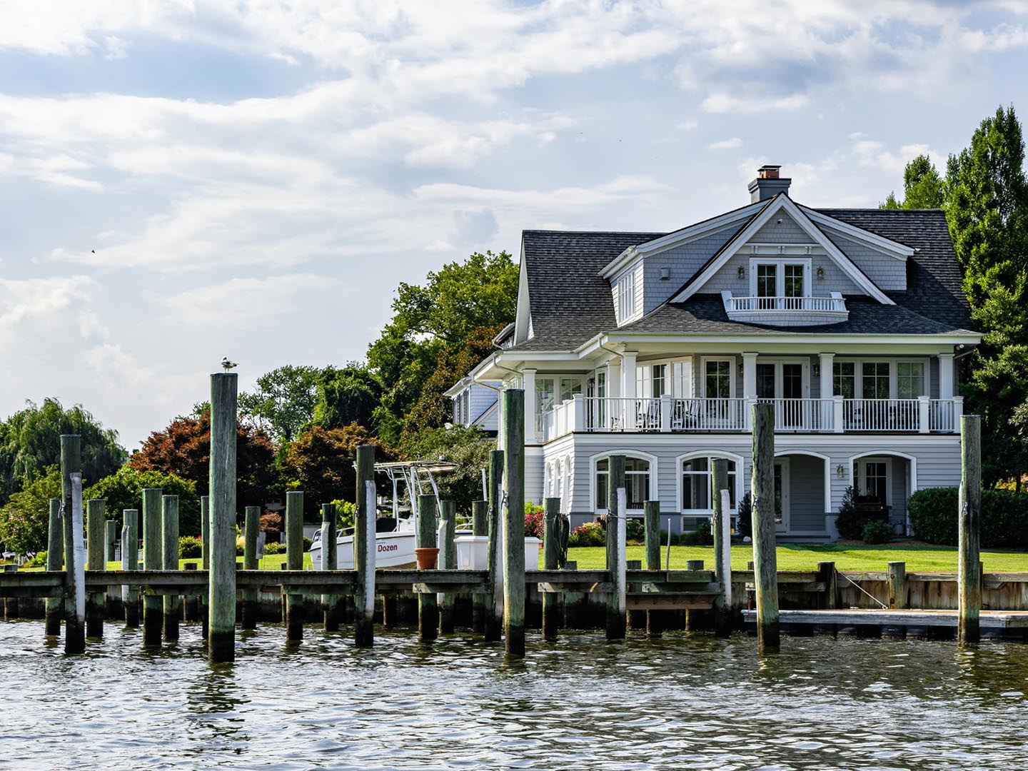 A three story blue and gray home on the water with a wooden dock on property.